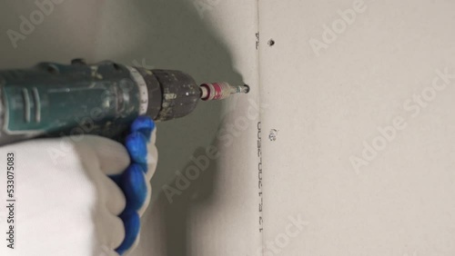 A worker with an accumulator screwdriver to tighten screws into a drywall panel, close-up