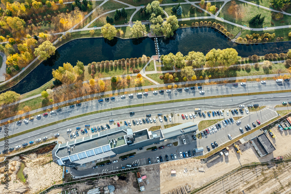 office building with parking lot near autumn park with water canal. aerial drone view.