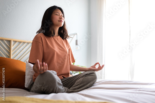 Young asian woman wearing comfortable clothes meditating on the bed in the morning to clear mind. Copy space.