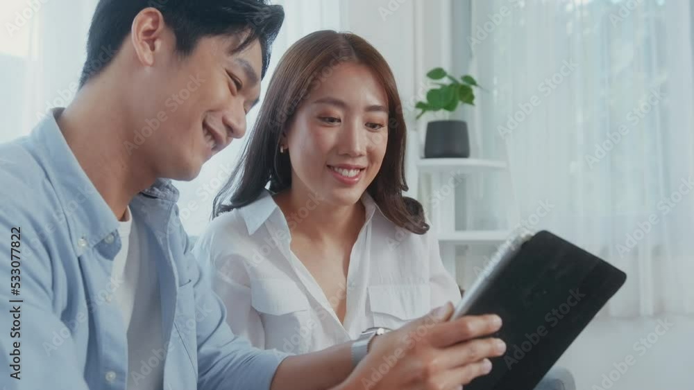 Young smiling asian couple playing social media in living room at home Young smiling asian couple playing social media in living room at home