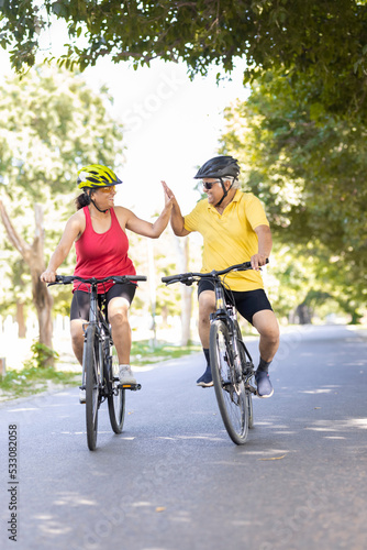 Active old man and woman giving high five while riding bicycle
