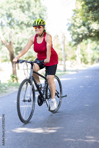 Happy old woman in sportswear riding bicycle outdoors on countryside road 