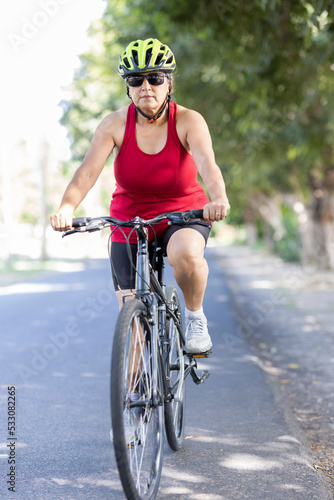 Happy old woman in sportswear riding bicycle outdoors on countryside road  © G-images