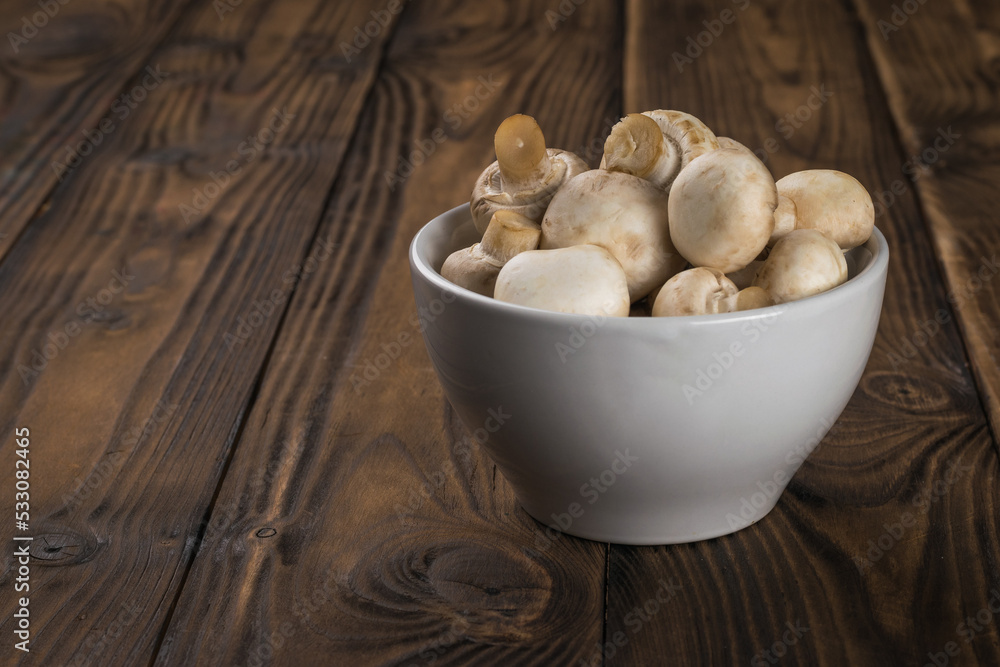 Small mushrooms in a white cup on a wooden table. Small mushrooms in a white cup on a wooden table.
