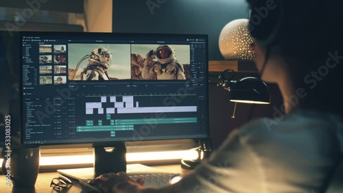 Male editor in headphones sitting at the table at night and editing video with astronauts for customer on pc in professional program while working remotely