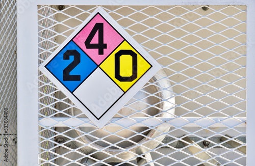 Liquid Petroleum gas cylinder stored horizontally in a metal safety cage with a Hazardous Materials Classification placard, eye level front view.