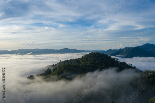 aerial view scenery sunrise above the mountain in tropical rainforest..slow floating fog blowing cover on the mountain look like as a sea of mist. .beautiful sunrise in the mist background. © Narong Niemhom