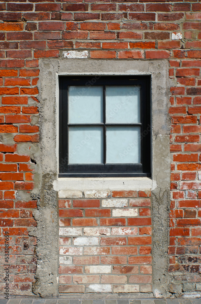 Close-up of a square paned window in an old red brick wall where a door used to be
