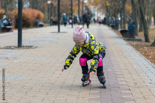 Cute little girl learns to roller skate. A child on roller skates falls photo