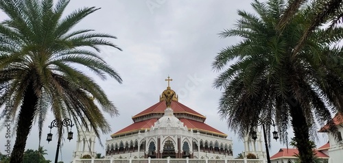 Famous and largest asian christian religion catholic church, chapel, cathedral, forane or shrine beautiful pilgrimage architecture building exterior in kerala india with palm trees and sky background.