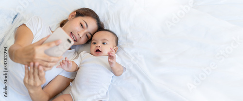 Authentic close up of asian mother and her newborn baby making a selfie or video call to father or relatives in a bed.Concept of technology,parenthood,family,connection,technology,Video Call. 
