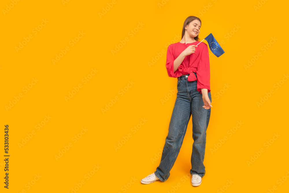Full-length portrait of young girl with the EU flag in her hands on orange background. Study in Europe. Copy space. Full-length portrait of young girl with the EU flag in her hands on orange background. Study in Europe. Copy space.