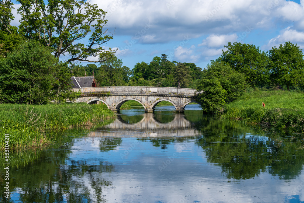 old stone bridge reflecting in a still river in green Irish countryside in spring
