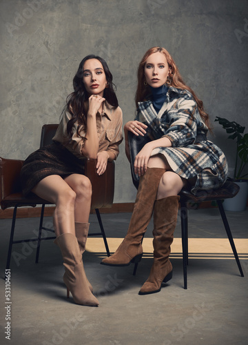Retro fashion: two beautiful young women sit on chairs. Vintage portrait of pretty girls in seventies style