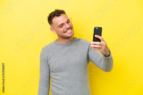 Young caucasian handsome man isolated on yellow background making a selfie © luismolinero