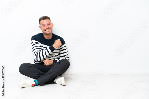 Young man sitting on the floor isolated on white background celebrating a victory