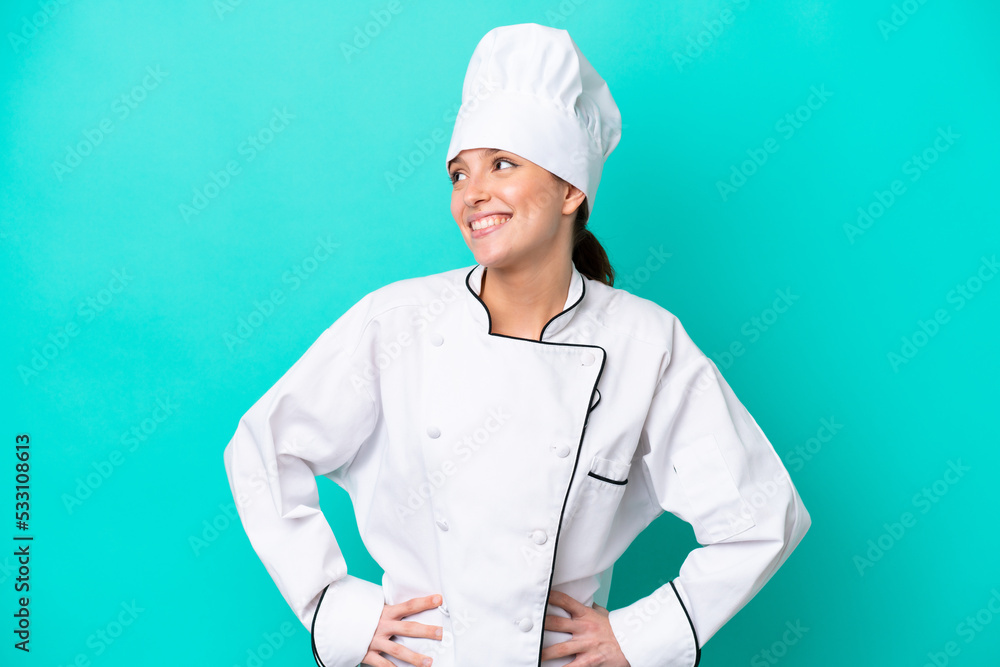 Young caucasian chef woman isolated on blue background posing with arms at hip and smiling Young caucasian chef woman isolated on blue background posing with arms at hip and smiling