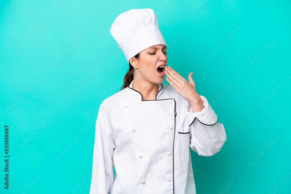 Young caucasian chef woman isolated on blue background yawning and covering wide open mouth with hand Young caucasian chef woman isolated on blue background yawning and covering wide open mouth with hand