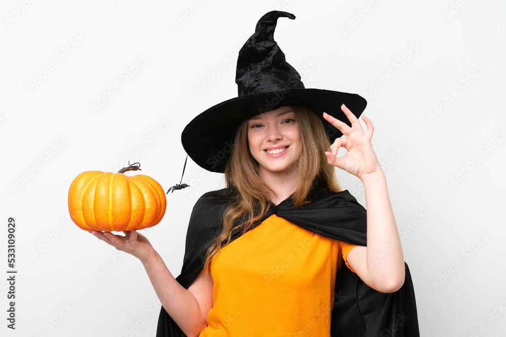 Young pretty woman costume as witch holding a pumpkin isolated on white background showing ok sign with fingers Young pretty woman costume as witch holding a pumpkin isolated on white background showing ok sign with fingers