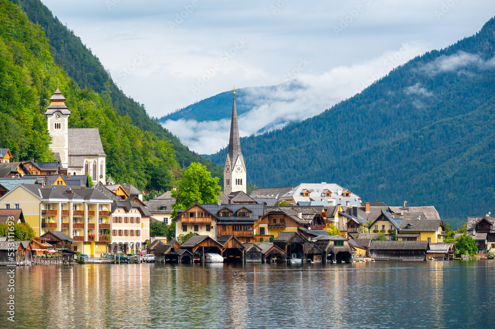 Hallstatt Village and Hallstatter See lake in Austria. Scenery with famous old church near the lake. Clouds and mist over the mountains in background. Famous tourist destination.