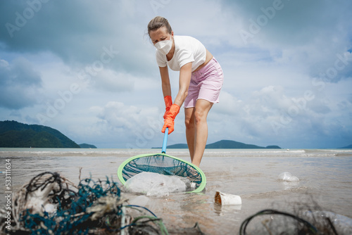 A female ecologist volunteer cleans the beach on the seashore from plastic and other waste