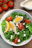 Delicious salad with boiled egg, tomatoes and cheese served on wooden table, flat lay