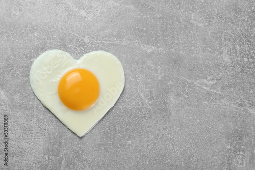 Heart shaped fried egg on light grey table, top view
