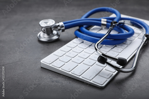 Computer keyboard with stethoscope on grey table, closeup