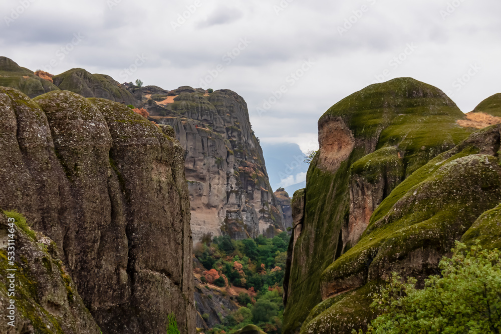 Panoramic morning view of unique rock formations near tourist village Kastraki on cloudy day in Kalambaka, Meteora, Thessaly, Greece, Europe. Rocks are overgrown with green moss. Moody atmosphere