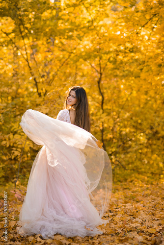 girl with long hair in a beautiful light fluffy dress is spinning in a yellow autumn forest