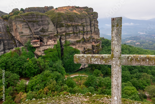 Cliff dwelling house or Ypapanti Monastery near Kalambaka seen from a hill with summit cross  Meteora  Thessaly  Greece  Europe. Built into cliff face  unreachable. Foggy rainy day mystical atmosphere