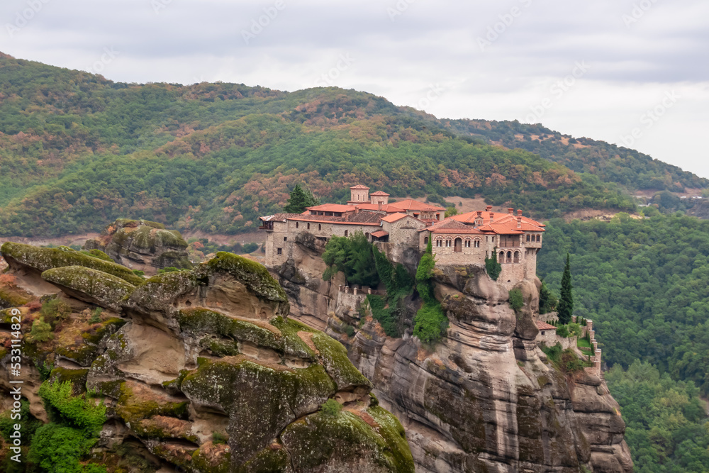 Scenic view of Holy Monastery of Varlaam on cloudy foggy day, Kalambaka, Meteora, Thessaly, Greece, Europe. Rock formations overgrown with green moss creating moody atmosphere. UNESCO World Heritage