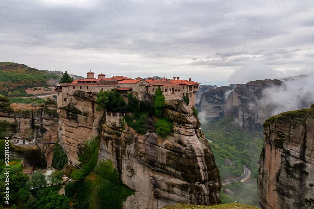 Fototapeta premium Scenic view of Holy Monastery of Varlaam on cloudy foggy day, Kalambaka, Meteora, Thessaly, Greece, Europe. Rock formations overgrown with green moss creating moody atmosphere. UNESCO World Heritage