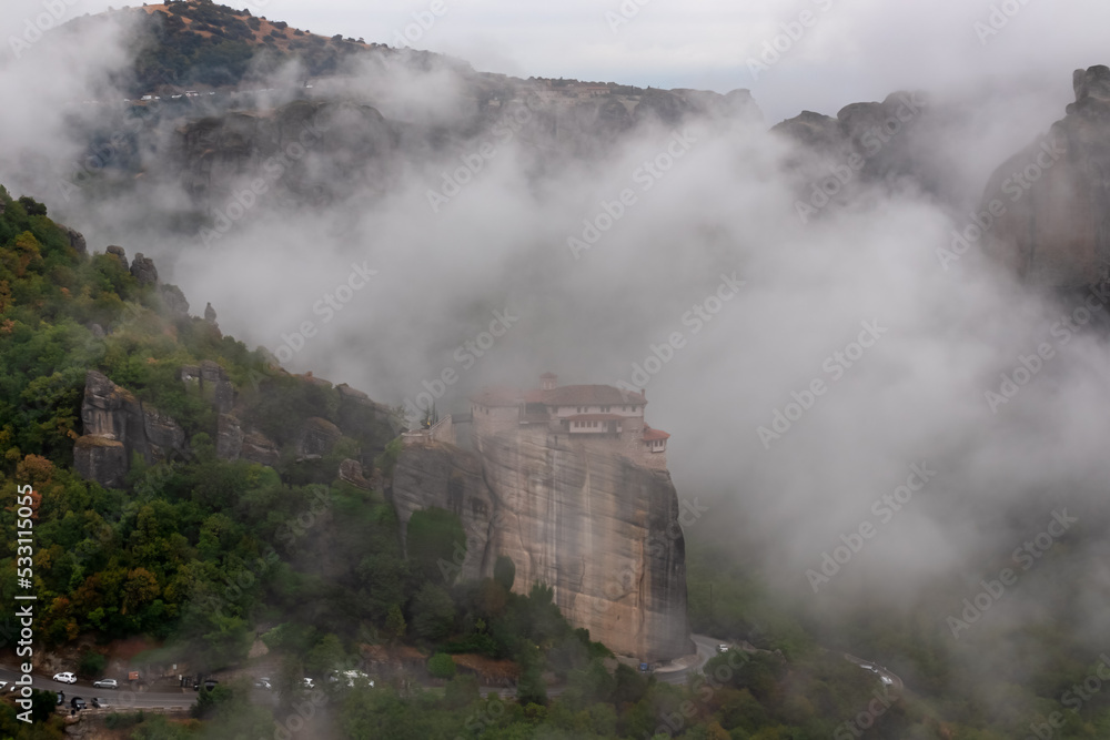 Scenic view of Holy Monastery of Rousanos appearing from the fog, Kalambaka, Meteora, Thessaly, Greece, Europe. Mystical atmosphere in dramatic landscape. Landmark build on unique rock formations