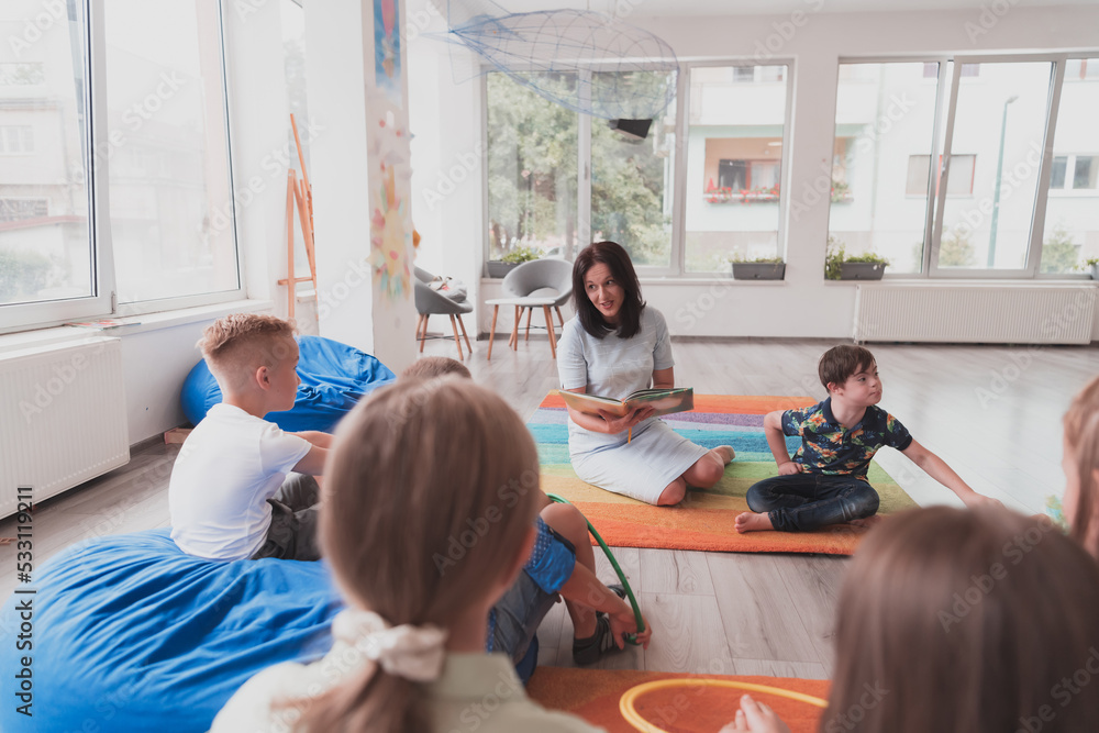 Obraz premium Reading time in an elementary school or kindergarten, a teacher reads a book to children in an elementary school or kindergarten. The concept of pre-school education. Selective focus