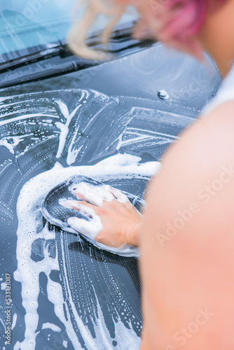 Blonde woman washes the hood of a car, rear view