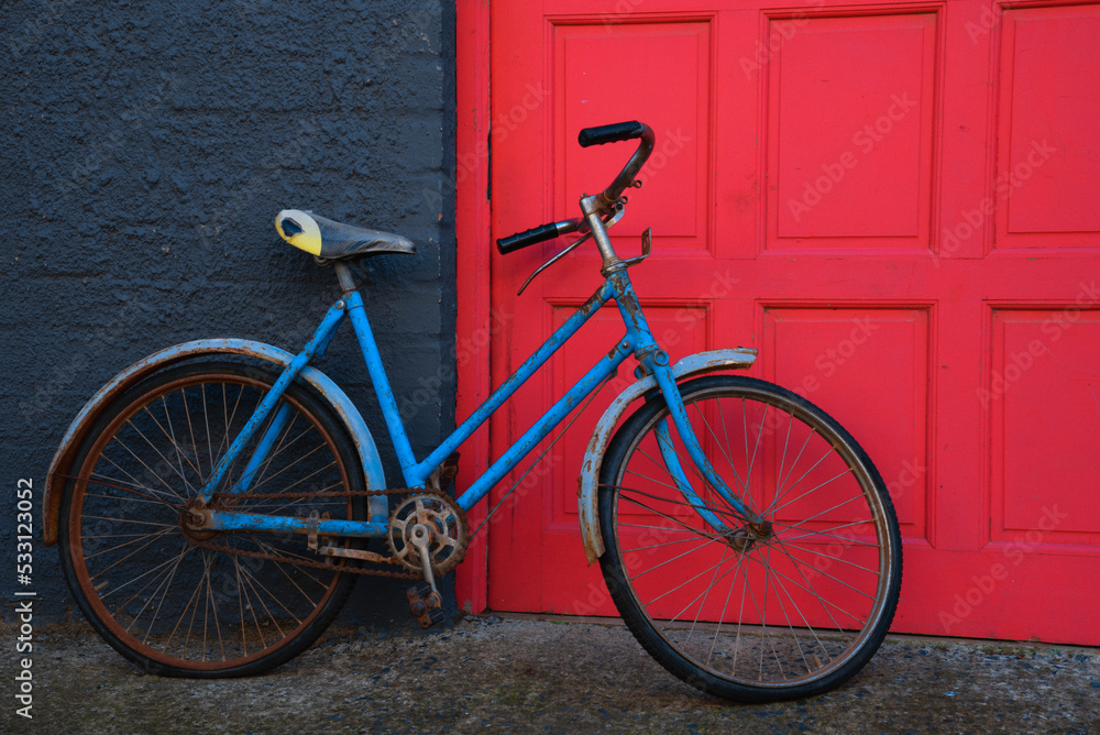 Old blue bicycle in front of a red door