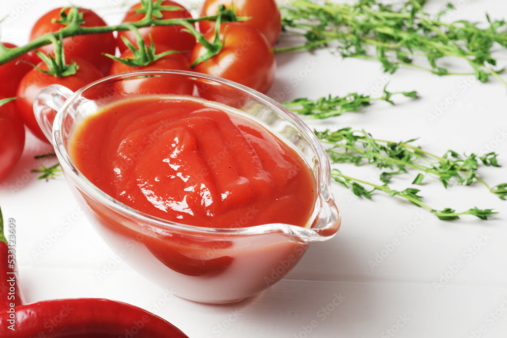 Gravy boat filled with delicious tomato sauce, a branch of fresh cherry tomatoes, thyme, fresh chilli on a wooden background. Gravy boat filled with delicious tomato sauce, a branch of fresh cherry tomatoes, thyme, fresh chilli on a wooden background.