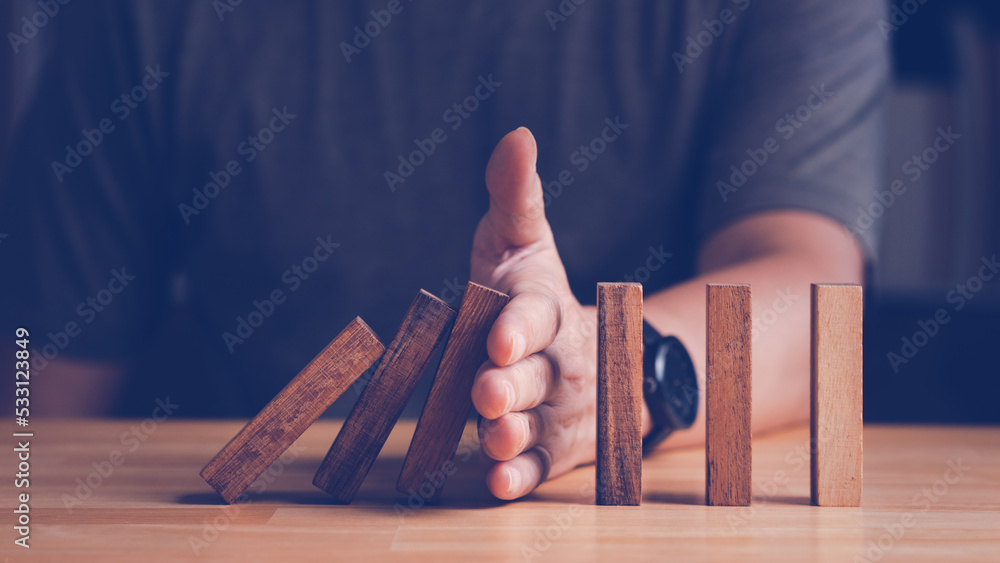 Risk assessment and management concept. Man's hand prevent or protect the domino wood block like risk that will impact or effect their business with good risk assessment. - obrazy, fototapety, plakaty 