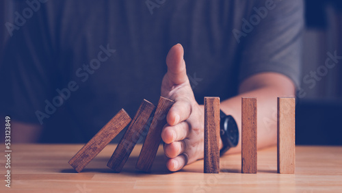 Risk assessment and management concept. Man's hand prevent or protect the domino wood block like risk that will impact or effect their business with good risk assessment. photo