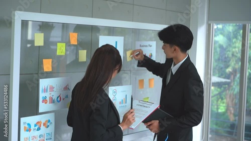 Businessman and Businesswoman is writing and brainstorming on glass board.