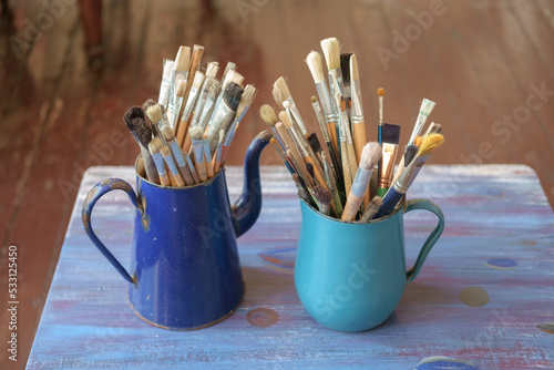 Various professional paint brushes in the blue metal jar on a blurred studio background, selective focus
