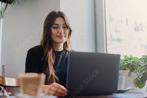 Girl typing on the keyboard. Beautiful young girl a laptop and smiling while sitting in cafe.