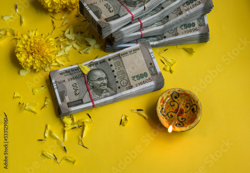 Plenty of Five Hundred Indian Rupee currency notes and traditional earthen Diwali lamp arranged with scattered marigold flowers. Hard currency is worshiped as Laxmi - a goddess of wealth.