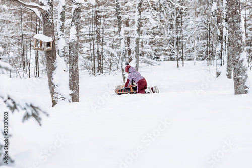 Happy little African-American girl in red hat and jumpsuit rides on tubing in the winter park.Beautiful trees are covered with white snow.Winter fun,active lifestyle concept.Selective focus,copy space