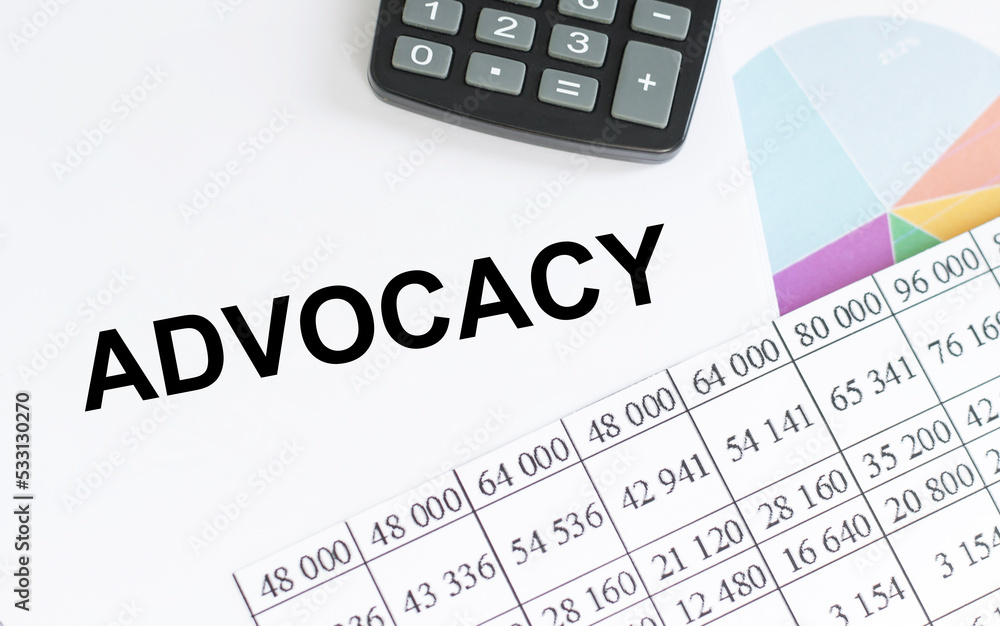 ADVOCACY inscription on a notebook next to reports and charts on the table ADVOCACY inscription on a notebook next to reports and charts on the table