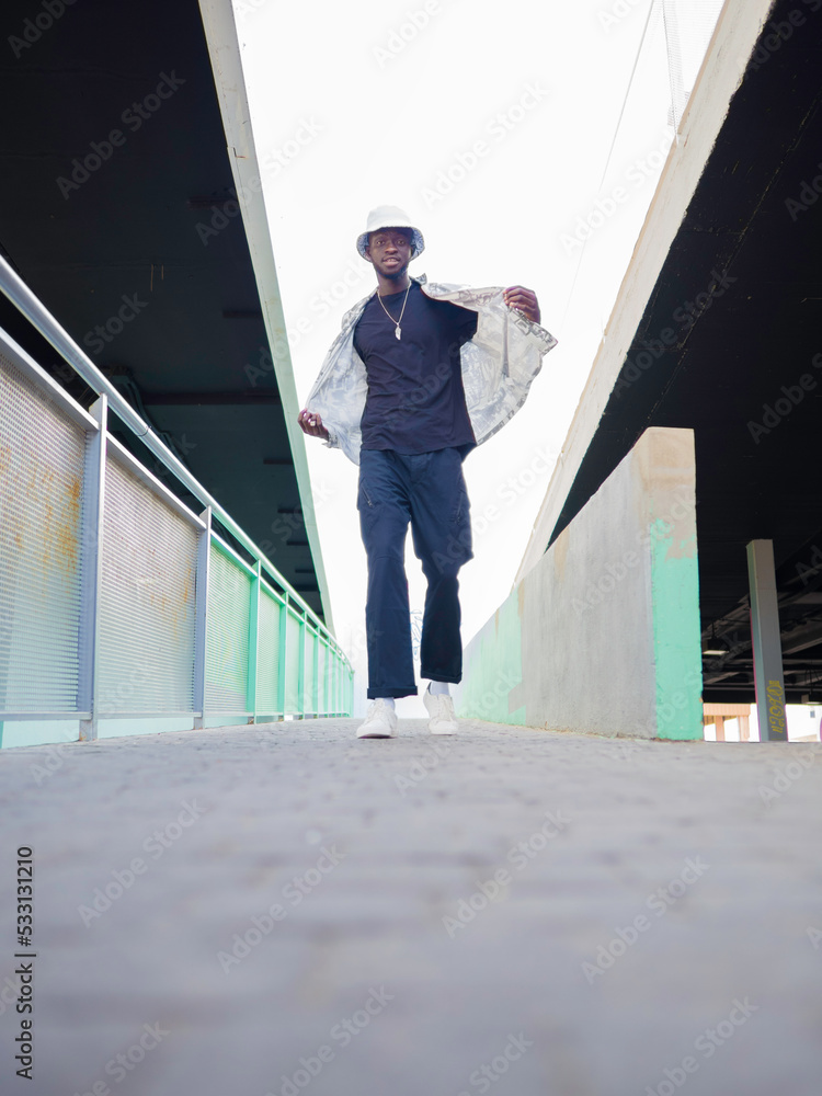 Young African American man walking and opening his shirt in an outdoor aisle of a shopping mall. Vertical photograph with copy space. Young African American man walking and opening his shirt in an outdoor aisle of a shopping mall. Vertical photograph with copy space.