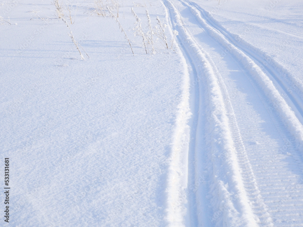 Track of traces from a snowmobile in drifts of white snow. Nature and outdoor on a winter sunny day. Background or backdrop