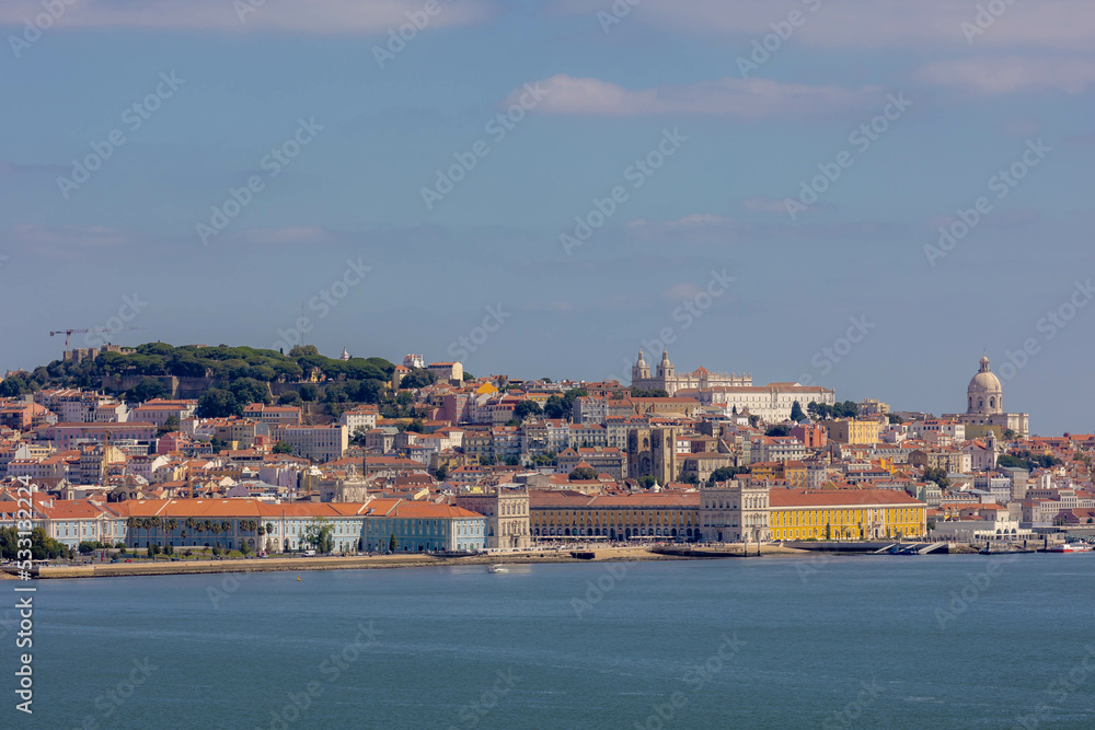 Summer cityscape of Lisbon from Almada side with blue sky, Orange brick roof top of buildings and housing with harbor view, Narrow houses on hilly in coastal of atlantic, The capital of Portugal.