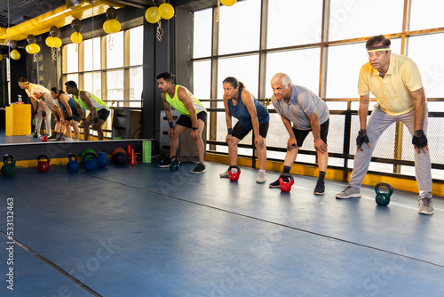 Men and woman exercising at health club with kettle bell on floor 